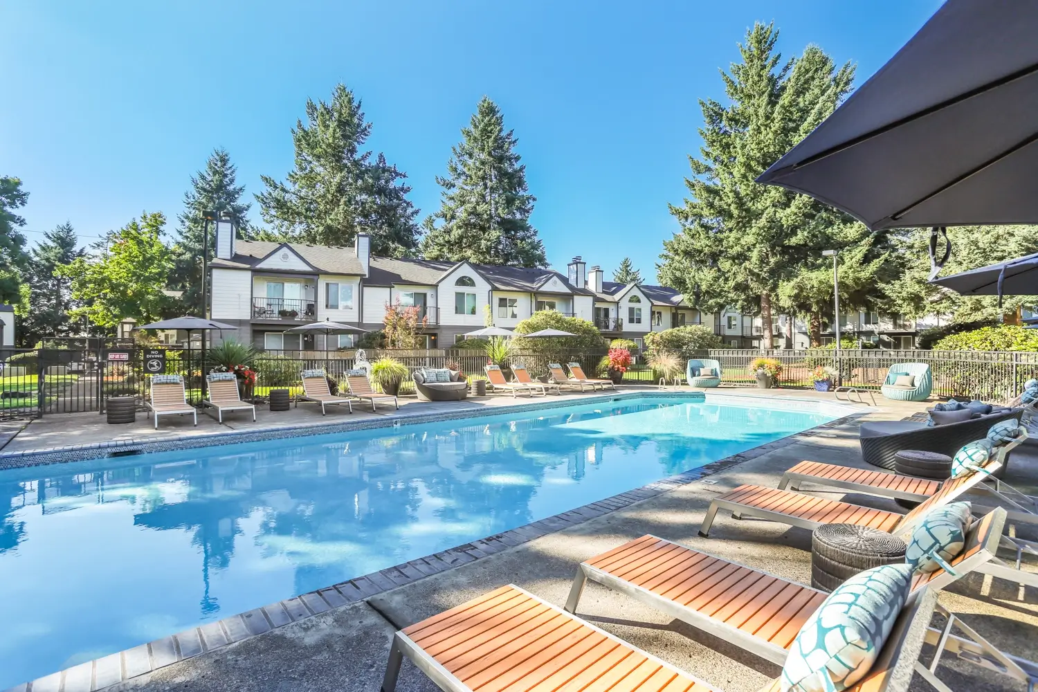 Outdoor pool area with comfortable seating, umbrellas for shade, and poolside lounge chairs.